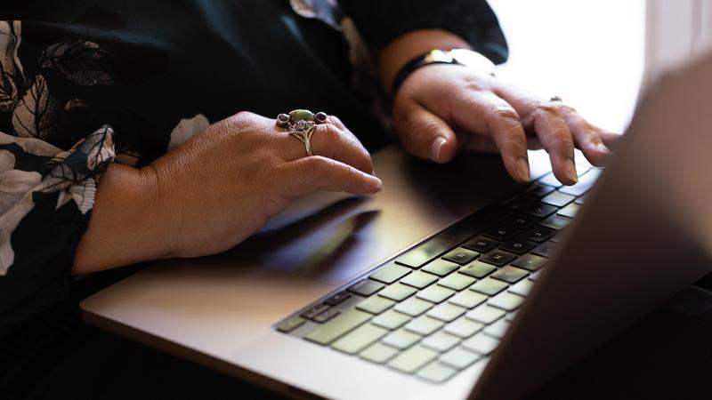 A person is shown their hands on a keyboard, wearing a floral blouse and rings .